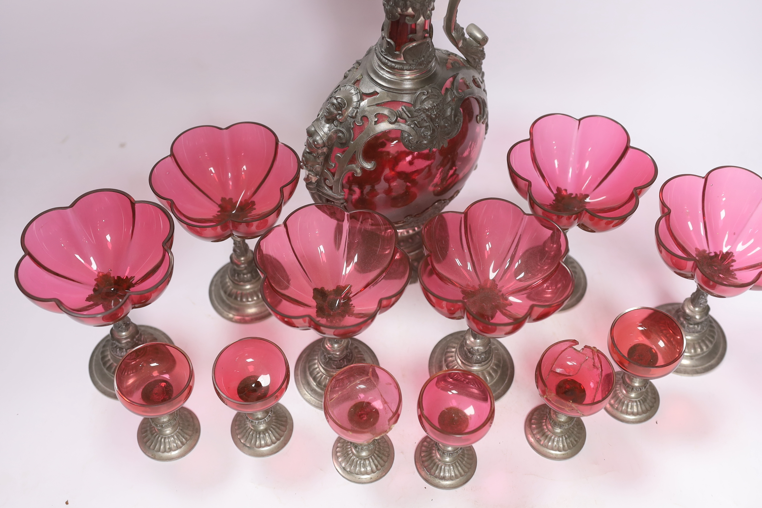 A Bohemian style pewter mounted cranberry glass ewer and twelve glasses, possibly Romanian, 33cm high